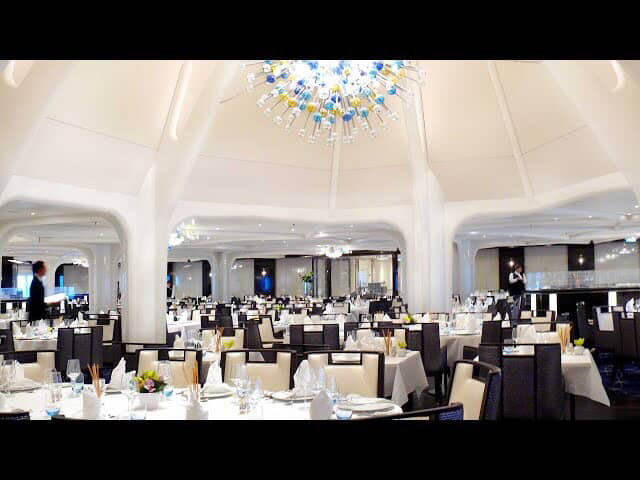 Elegant cruise ship dining room with tables and a modern chandelier.