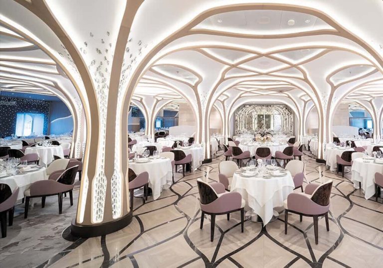Elegant cruise ship dining room with white tablecloths and arched ceilings.