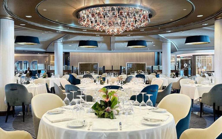 Elegant cruise ship dining room with chandelier and set tables.