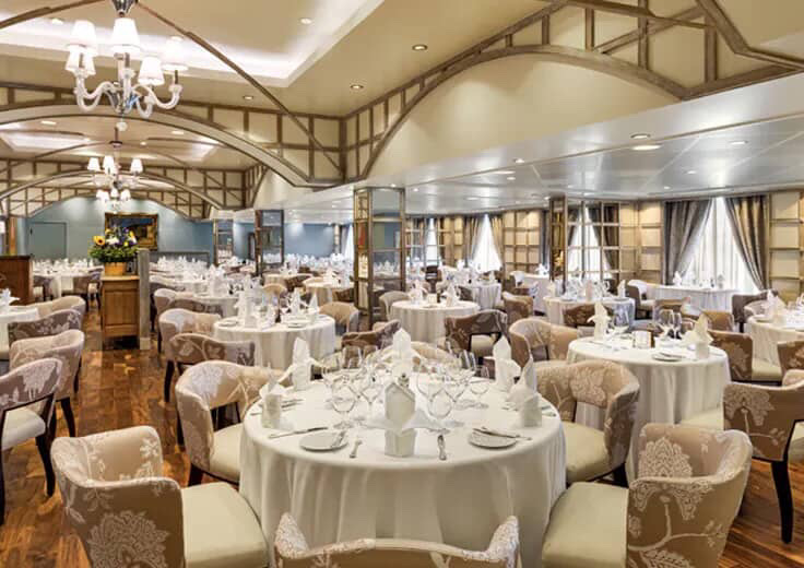 Elegant cruise ship dining room with set tables and upholstered chairs.