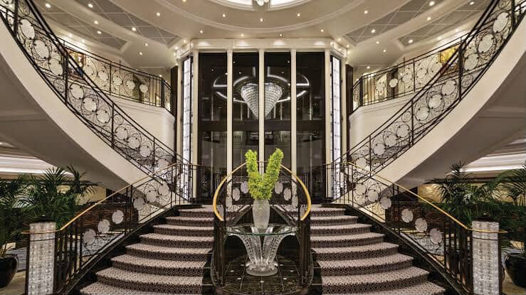 Elegant cruise ship grand staircase with floral centerpiece and ornate railings.