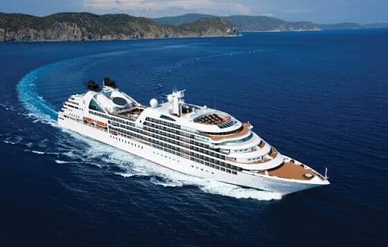 Cruise ship sailing on blue sea with green coastline in background.