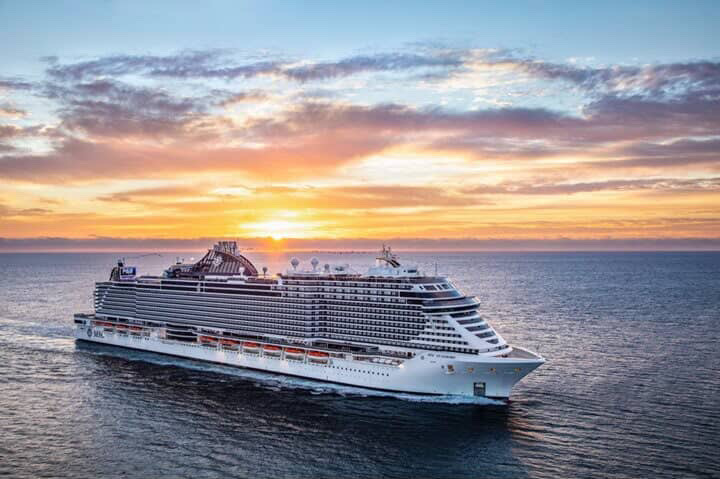 Large cruise ship sailing on the ocean at sunset with colorful sky in background.