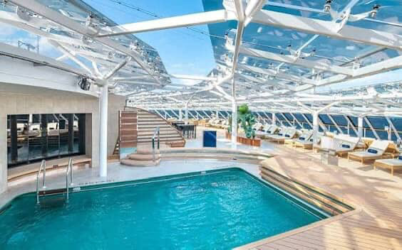 Cruise ship pool deck with retractable roof and lounge chairs.