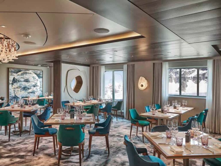 Elegant cruise ship restaurant interior with tables, chairs, and mountain view.