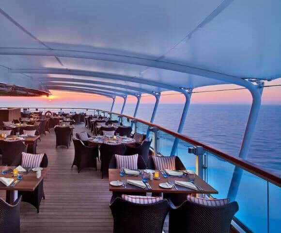 Outdoor cruise ship restaurant at sunset with ocean view.