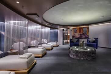 Cruise ship spa relaxation area with beds and seating.