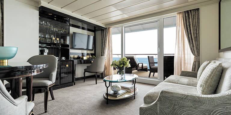 Cruise suite interior with seating area, balcony, and ocean view.