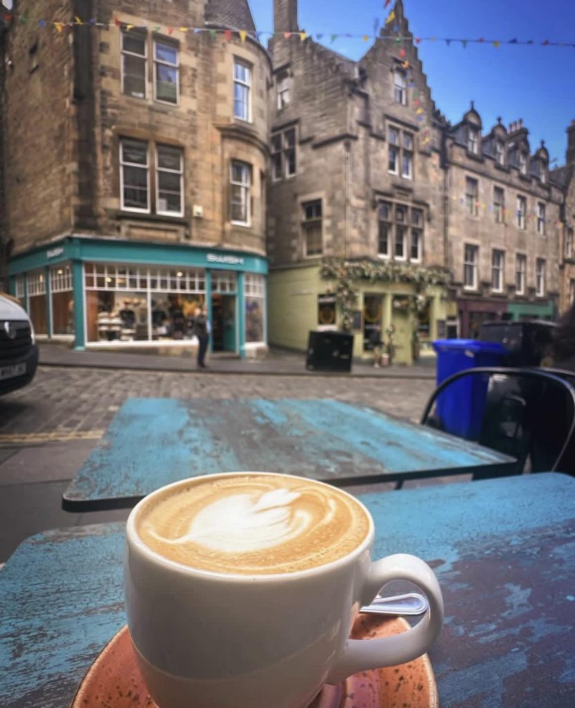 Coffee cup with latte art on a rustic table, Edinburgh street scene background
