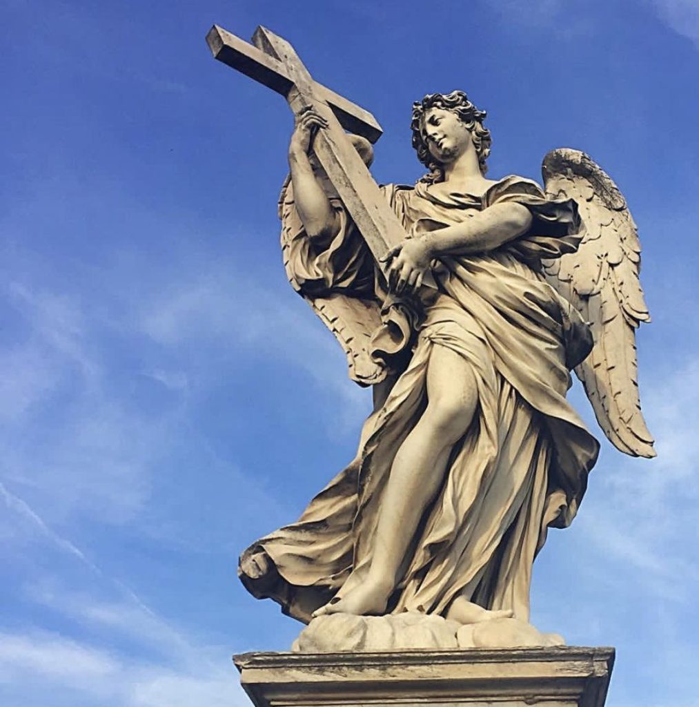 Angel statue holding a cross against a blue sky