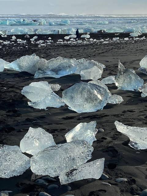 Glacial ice chunks on a black sand beach with waves in the background.