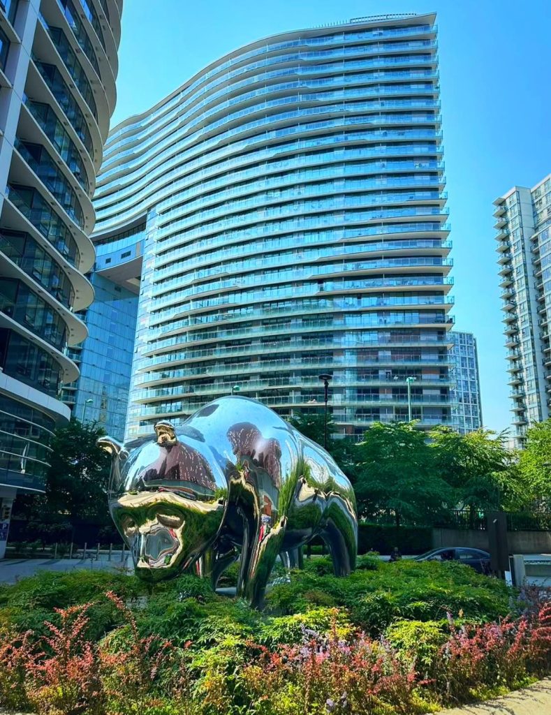 Chrome bull sculpture in front of modern glass buildings with blue sky