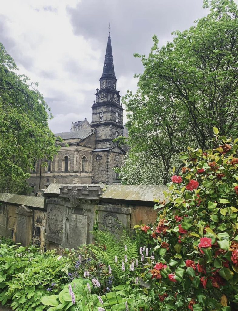 Tombstones and lush greenery in front of a historic church with a clock tower