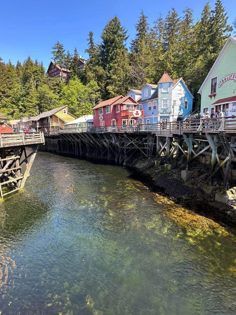 Colorful buildings on stilts over a clear waterway in a forest setting.
