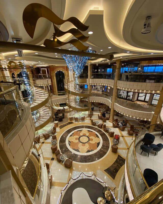 Grand atrium with spiral staircases and a large chandelier on a cruise ship