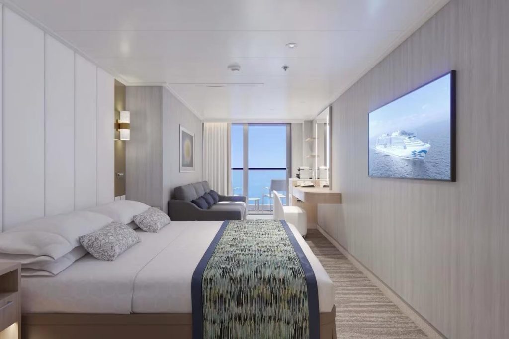Modern cruise ship cabin with bed, sofa, desk, and ocean view balcony.