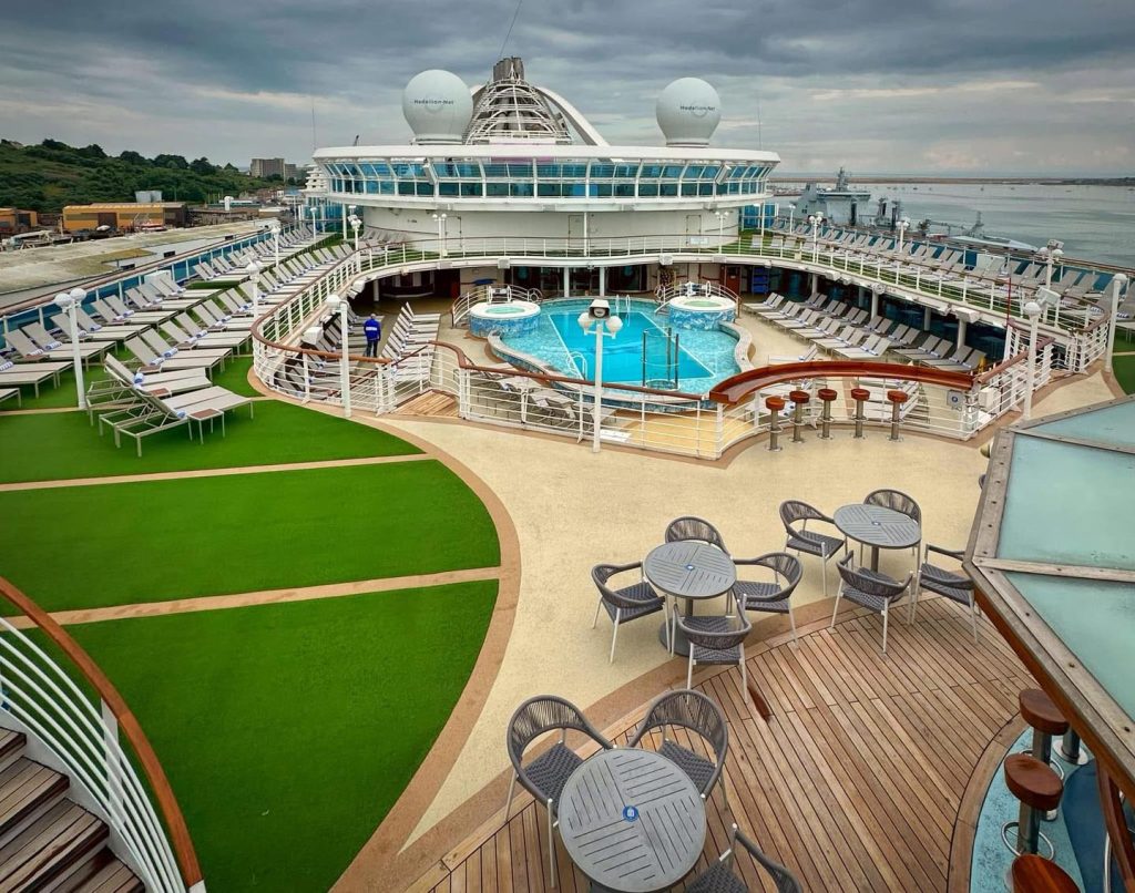 Cruise ship deck with pool, lounge chairs, and outdoor seating areas.