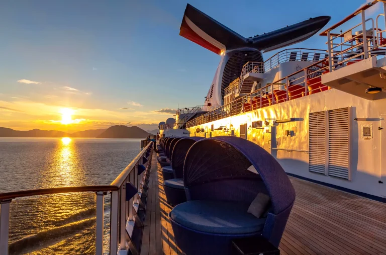 Cruise ship deck with lounge chairs at sunset over the ocean.