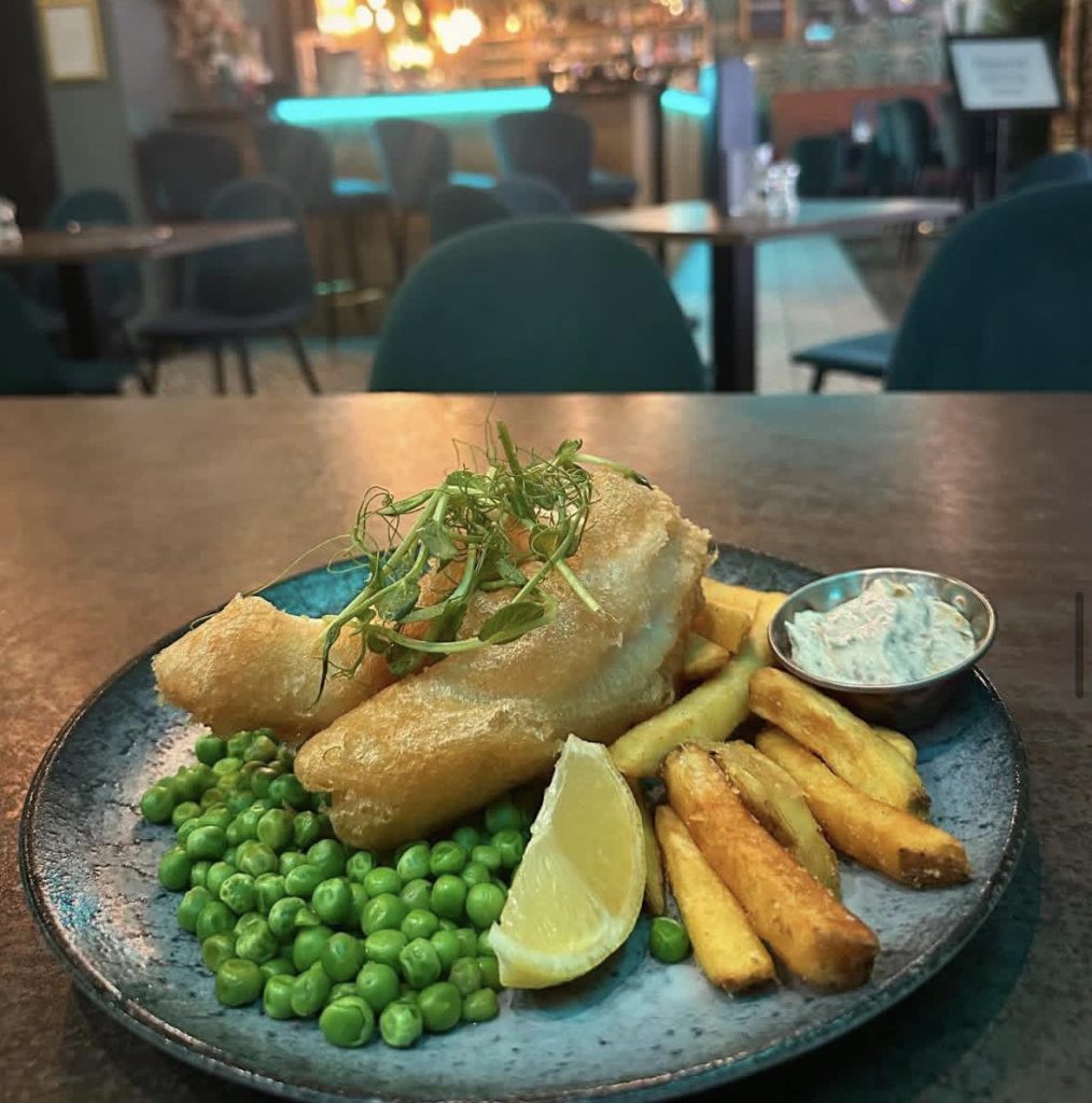 Battered fish and chips with peas and tartar sauce on a dark plate.