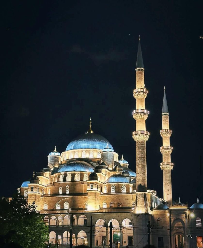 New Mosque (Yeni Cami) in Istanbul illuminated at night, with blue domes and tall minarets.