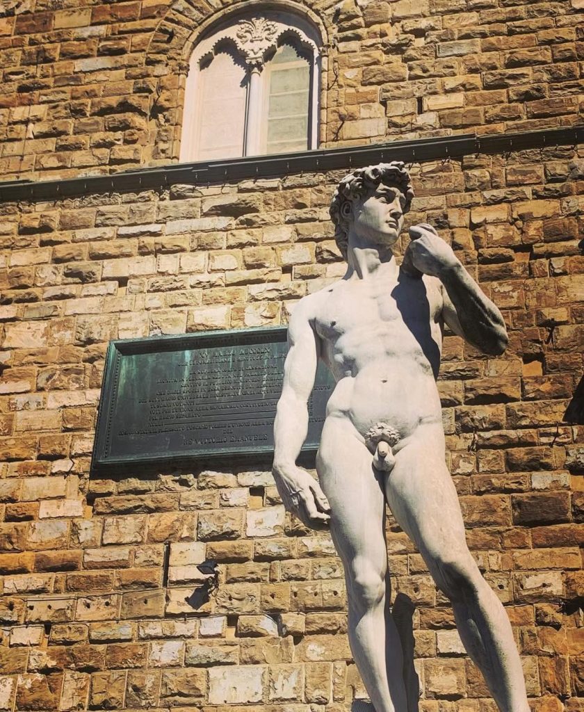 Michelangelo's David statue stands against a stone building in Florence, Italy.