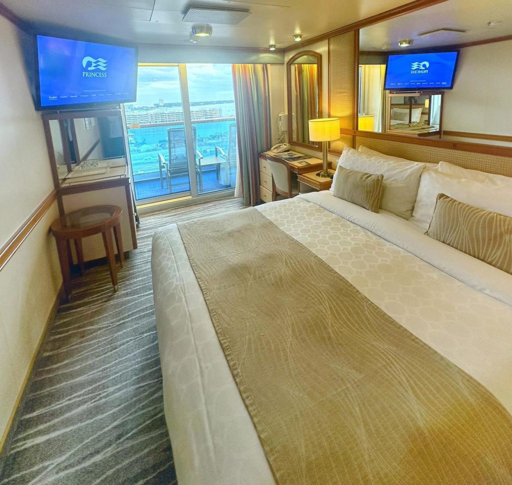 Princess cruise ship cabin with balcony, desk, and TV showing Princess Cruises logo