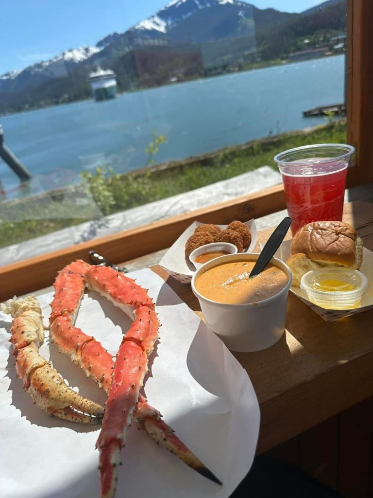 King crab legs, soup, fried food, and a drink with a scenic waterfront view.