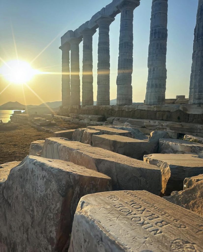 Temple of Poseidon at sunset, with fallen columns and inscribed stones.
